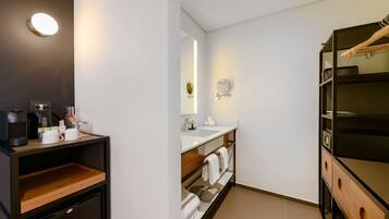 A modern bathroom with a built-in sink, mirror, and towel rack. There is a coffee maker and a shelf with toiletries.