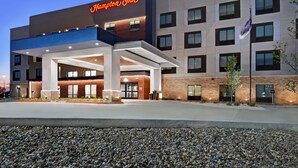 Un hotel Hampton Inn con diseño moderno, que destaca por su entrada principal, varios pisos y una fachada bien iluminada.
