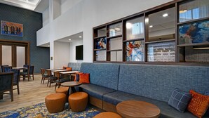 Un moderno vestíbulo de hotel con una zona de estar, mesas de madera y una gran pared decorada con obras de arte.