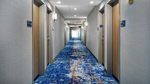 Pasillo de hotel con alfombra azul, puertas a ambos lados e iluminación del techo.