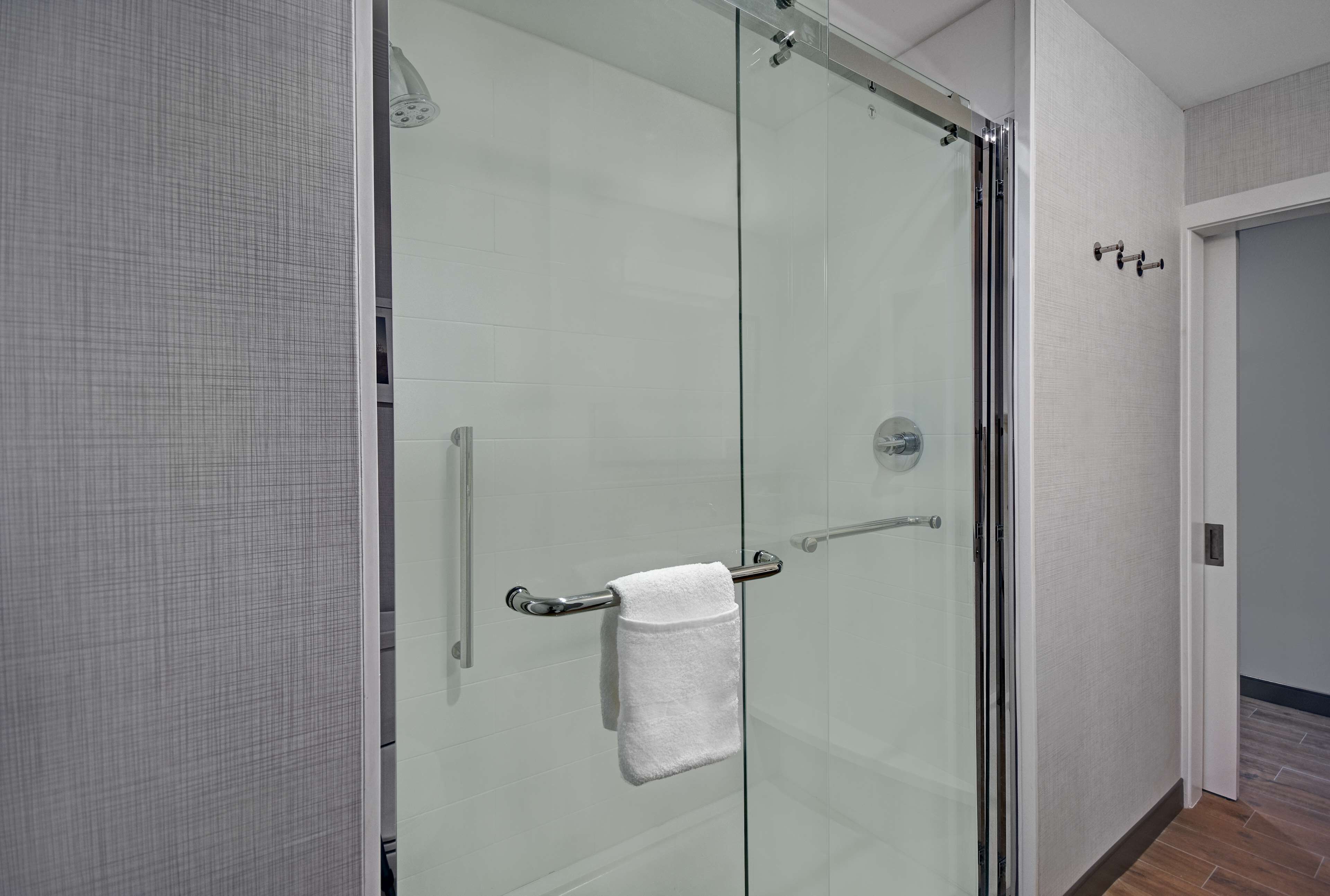 A modern bathroom with a glass shower enclosure, a towel rack, and a visible door handle.