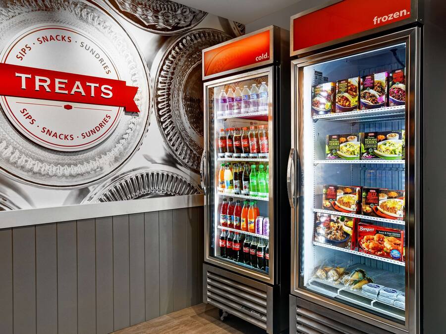 Una pared con un letrero circular que dice "TREATS" y dos vitrinas refrigeradas llenas de bebidas y alimentos.