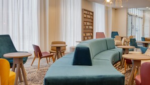 A modern lounge area with a teal sofa, wooden bookshelves, and a variety of seating options including chairs and tables.