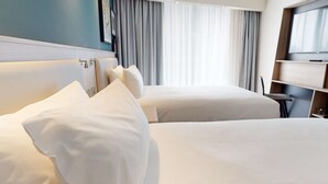A hotel room with two beds, a desk, and a TV.