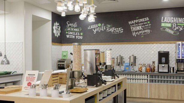 Un café moderno con mostrador, máquinas de café y una pared con citas motivacionales.