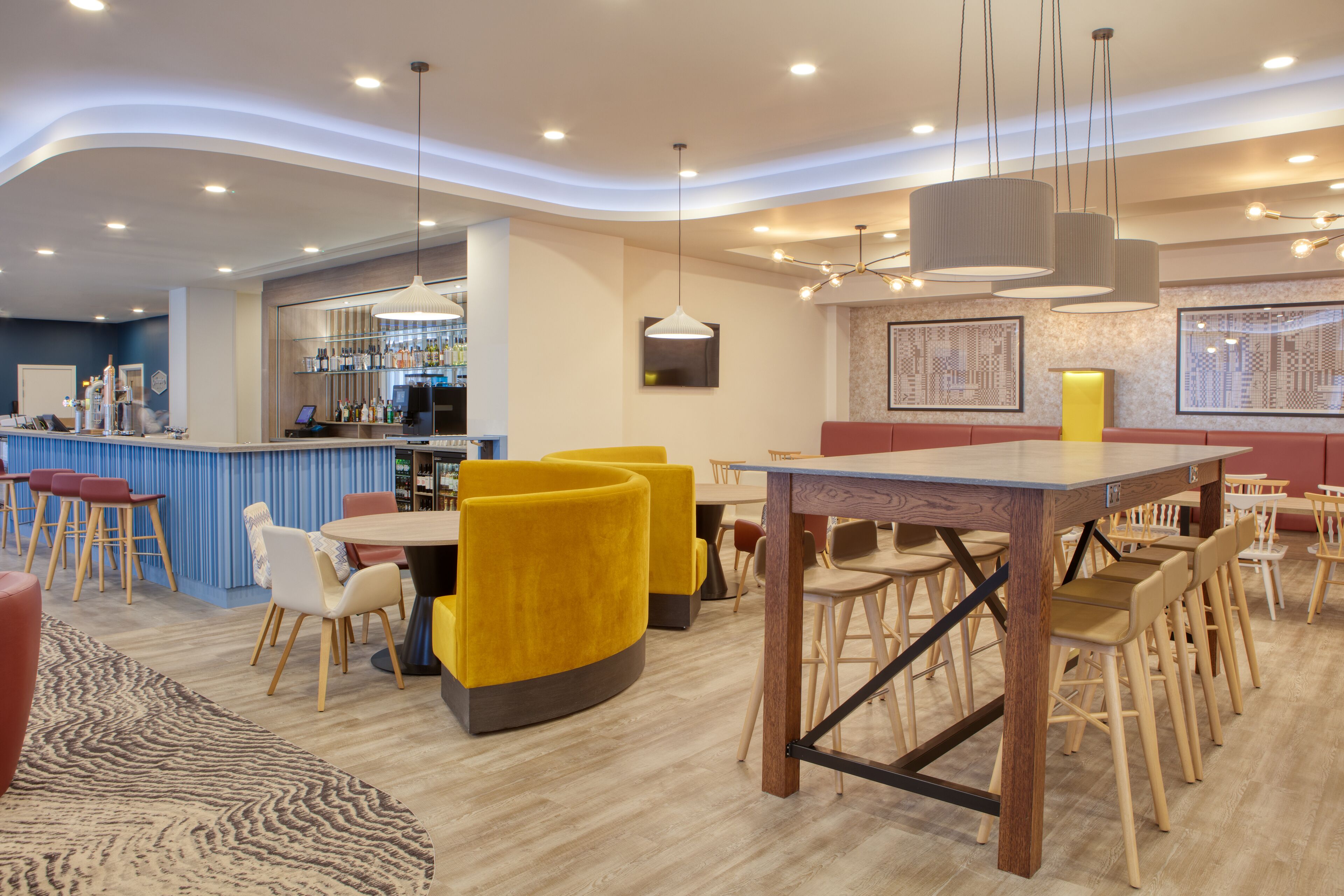 A modern restaurant with yellow chairs, a bar area, and a wooden dining table.