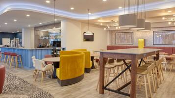 A modern restaurant with yellow chairs, a bar area, and a wooden dining table.