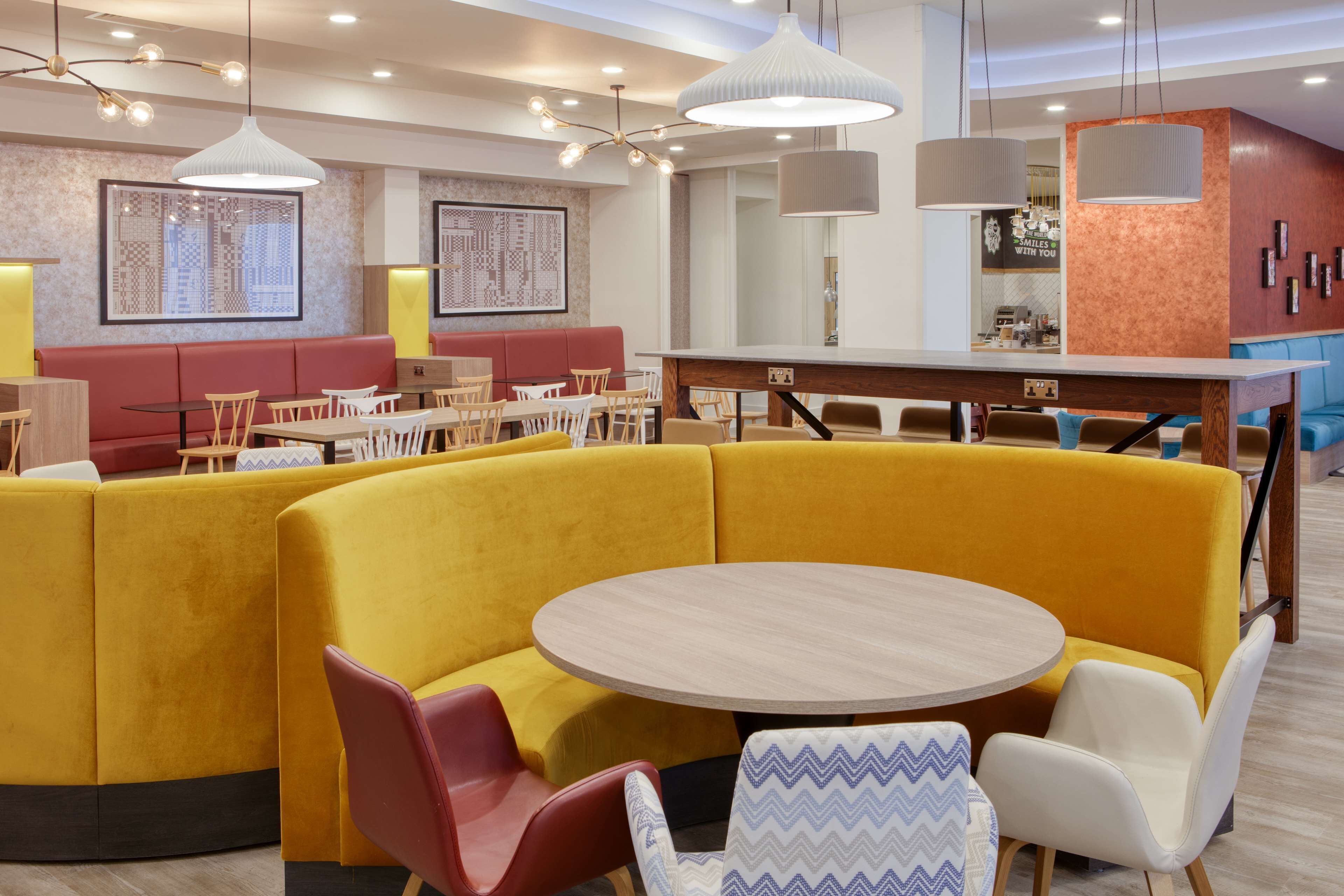 Un restaurante moderno con asientos tipo banca amarillos, mesas de madera e iluminación colgante.