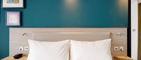 A hotel room with a bed, two bedside tables, a wall-mounted phone, and two framed pictures.
