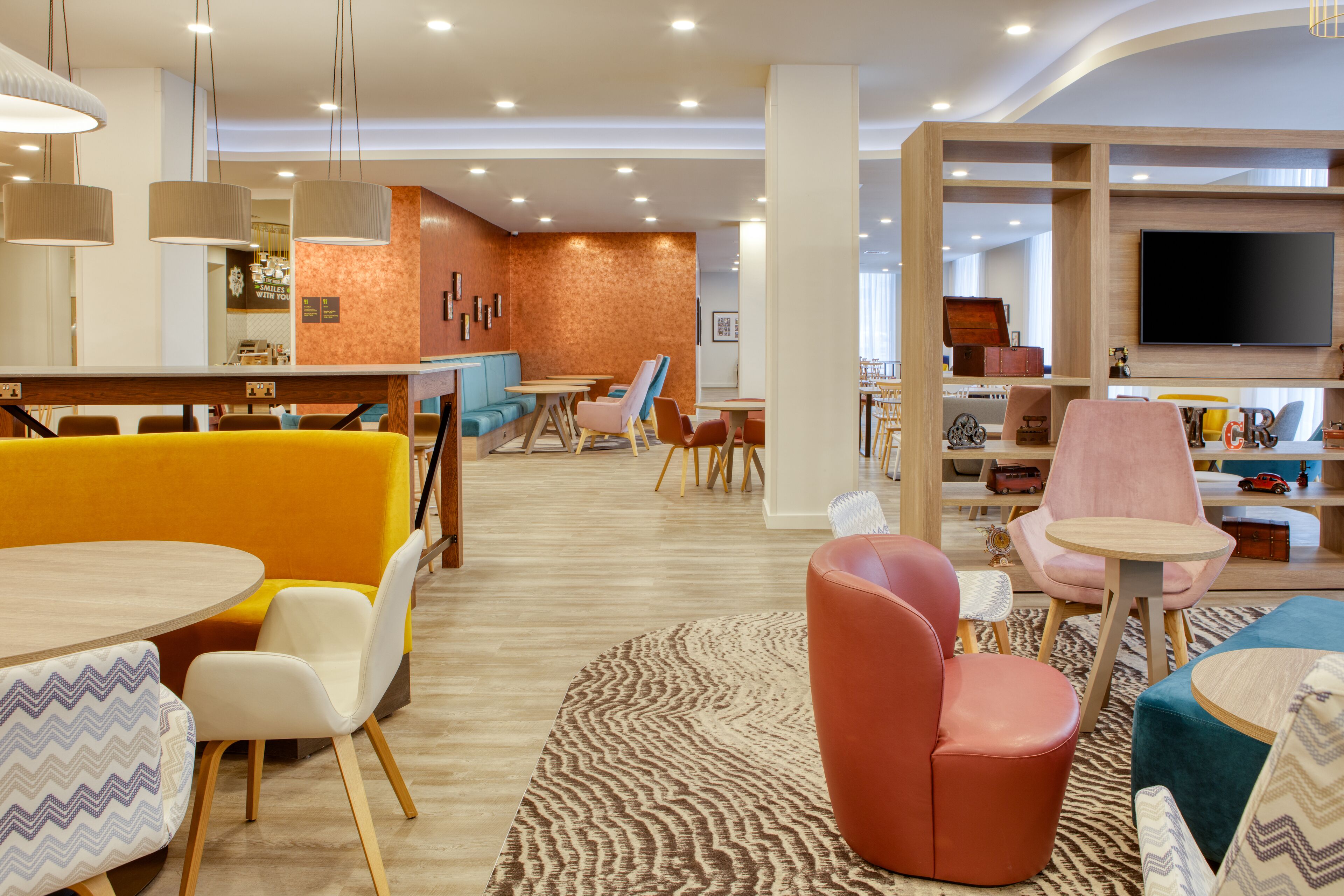 A modern hotel lobby with seating areas, a bar, and a television.