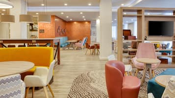 Um hall de hotel moderno com áreas de estar, um bar e uma televisão.