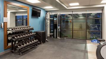A gym with weight racks, a mirror, a television, and a window with a view of the outside.
