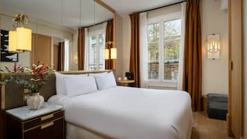 A hotel room with a large bed, a bedside table, a mirror, a window with curtains, and a view of the outside.