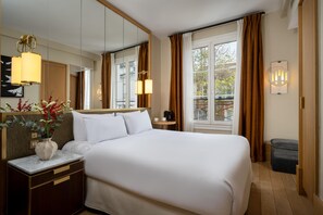 A hotel room with a large bed, a bedside table, a mirror, a window with curtains, and a view of the outside. - Le Belgrand Hotel Paris Champs Elysees, Tapestry by Hilton (Paris)