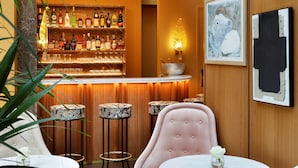 A bar area with wooden paneling, a bar counter with bottles, and two round tables with chairs. - Le Belgrand Hotel Paris Champs Elysees, Tapestry by Hilton (Paris)