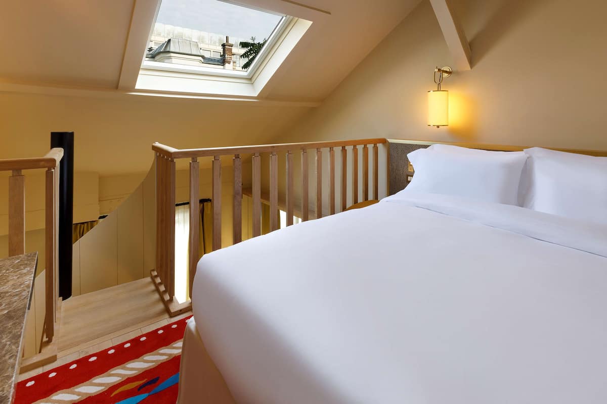 A bedroom with a skylight, a wooden staircase, and a bed with white bedding.