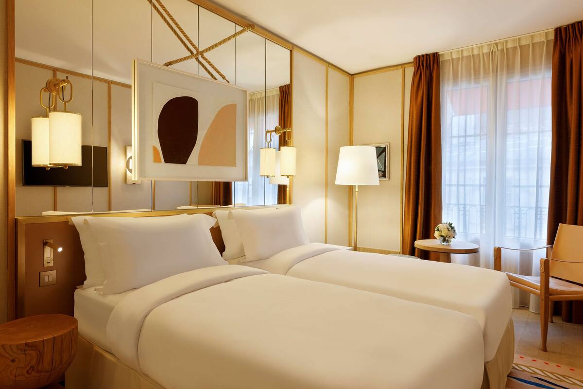 A hotel room with two beds, a large mirror, a flat-screen TV, a small table with a vase, and a chair.