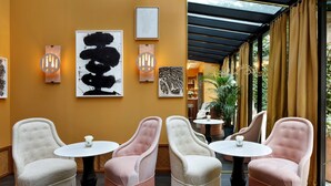 A modern interior with four upholstered chairs and small round tables, a yellow wall with framed artwork, and a glass-enclosed area with curtains. - Le Belgrand Hotel Paris Champs Elysees, Tapestry by Hilton (Paris)