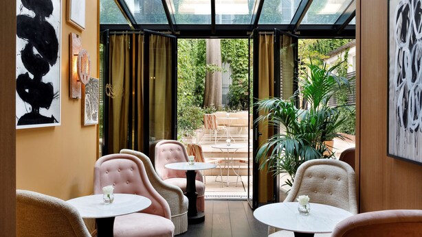 A cozy indoor seating area with cushioned chairs and round tables, a glass ceiling, and artwork on the walls. - Le Belgrand Hotel Paris Champs Elysees, Tapestry by Hilton (Paris)