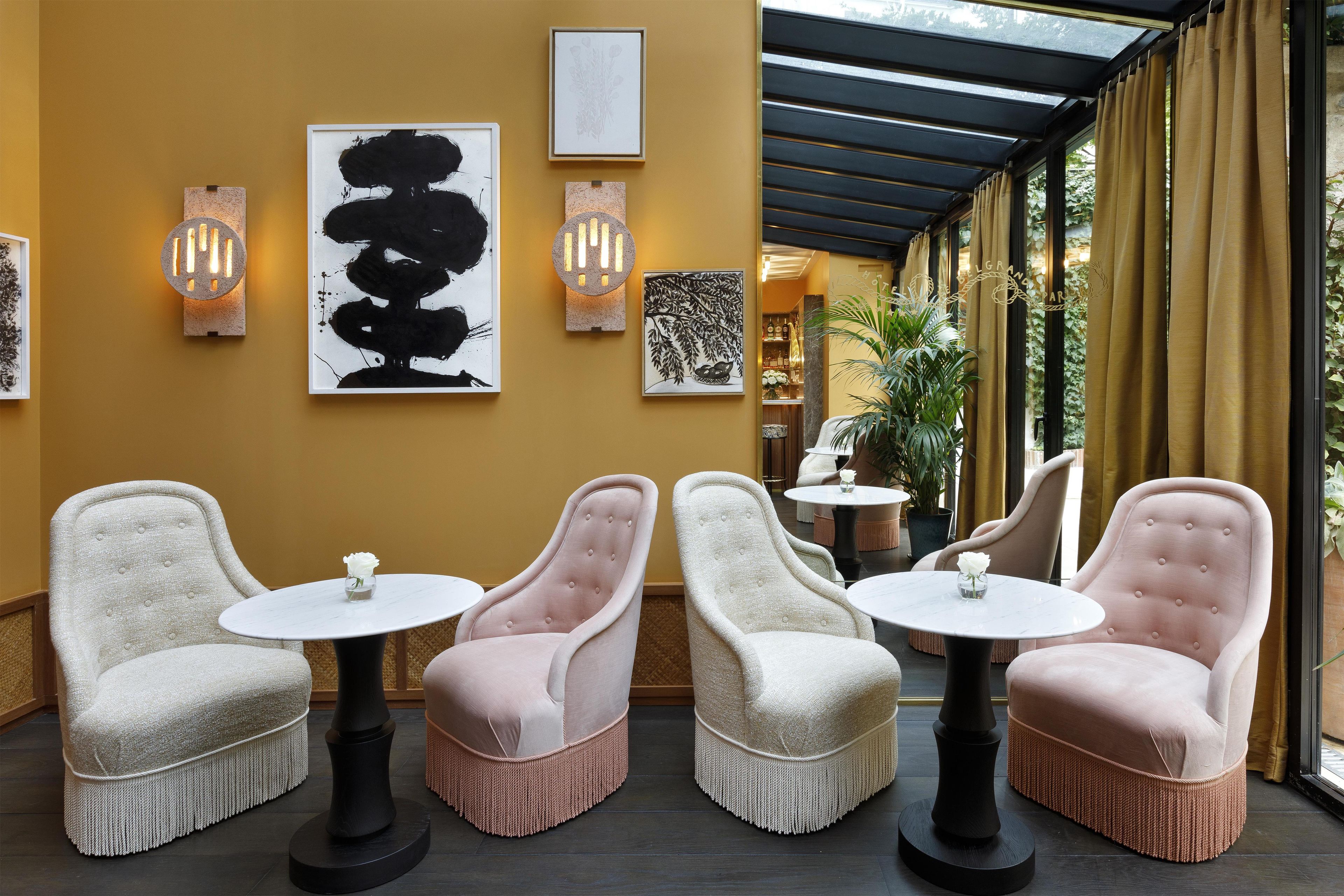 A seating area with four upholstered chairs and round tables, a wall with framed artwork, and a glass door leading to an outdoor space.