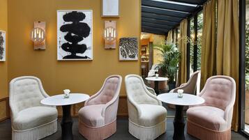 A seating area with four upholstered chairs and round tables, a wall with framed artwork, and a glass door leading to an outdoor space.