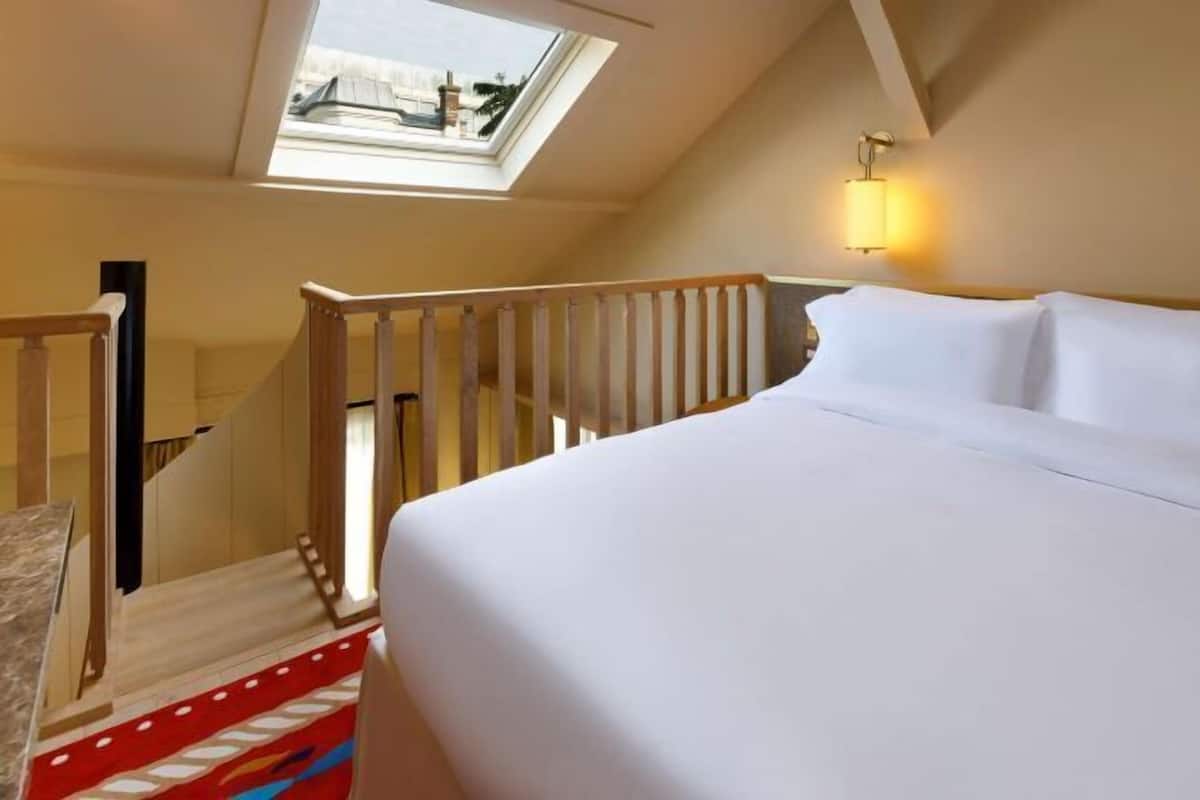 A hotel room with a skylight, a bed, a staircase, and a wall-mounted light fixture.