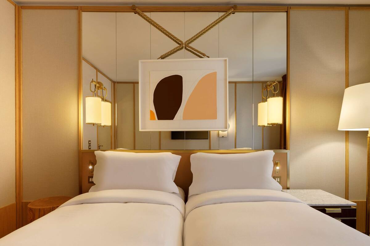 A hotel room with a large bed, a bedside table, a mirror, and a framed artwork above the bed.