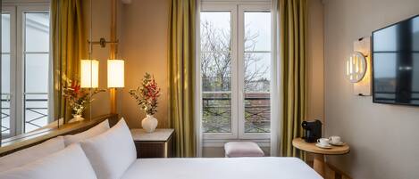 A hotel room with a large bed, a bedside table with a lamp, a small table with a coffee maker, and a TV mounted on the wall.