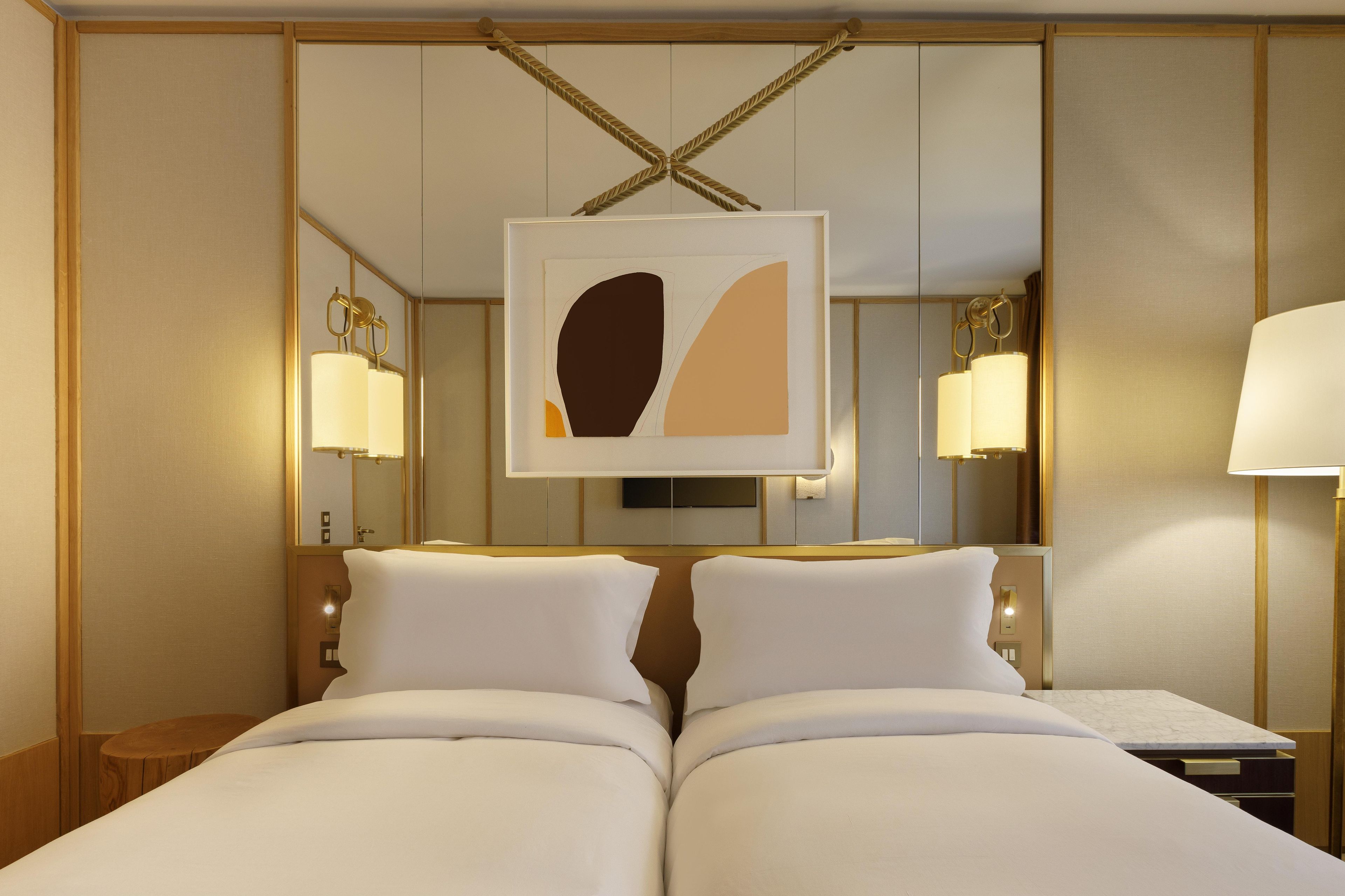 Una camera d'albergo con un letto matrimoniale, lampade ai comodini, uno specchio grande e un'opera d'arte appesa al muro.