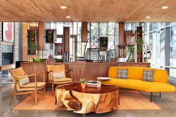 A modern bar area with a central island, surrounded by bar stools and a seating area with wicker chairs and a sofa. at Canopy by Hilton Tempe Downtown