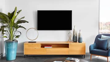 Ein modernes Wohnzimmer mit einem Holz-TV-Schrank, einem blauen Sessel, einem runden Couchtisch und einer großen Topfpflanze.
