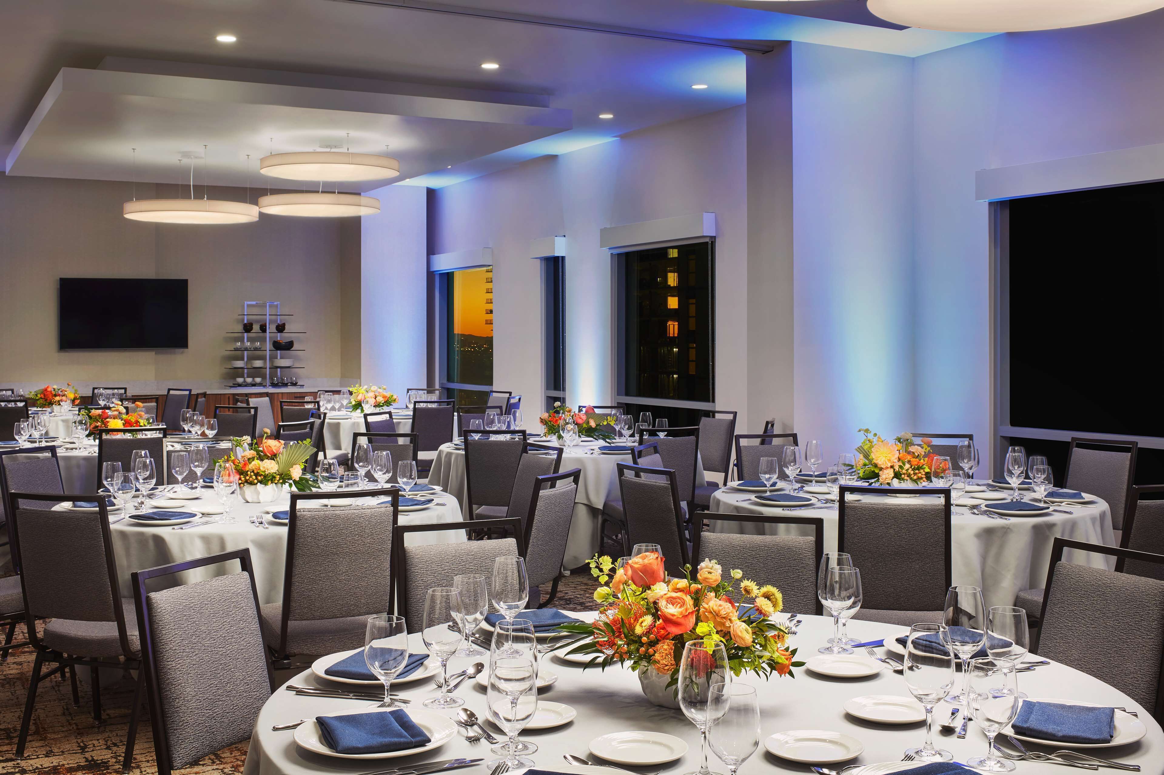A banquet hall with round tables set for dining, equipped with chairs, plates, cutlery, and glasses.