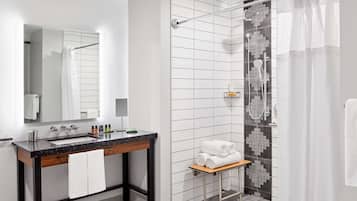 Une salle de bain moderne avec un lavabo en marbre, un miroir, une douche avec une porte en verre et un petit banc avec des serviettes.