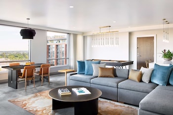 A modern bedroom with a large bed, a desk, and a chair. There is a window with a view of buildings, a lamp, and artwork on the wall. at Canopy by Hilton Tempe Downtown