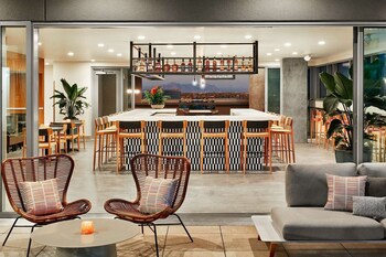 A modern restaurant with a bar area, seating with round tables and bar stools, and decorative plants. at Canopy by Hilton Tempe Downtown