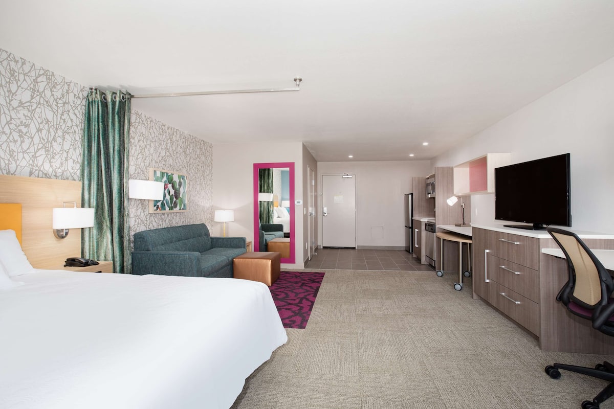 A hotel room with a bed, a desk, a television, and a bathroom visible through an open door.
