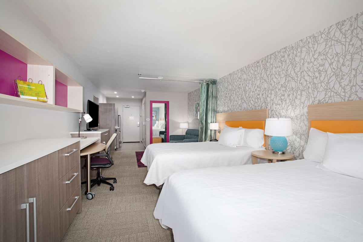 A hotel room with two beds, a desk with a computer, a chair, and a small table with a lamp.