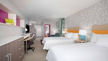 A hotel room with two beds, a desk with a computer, a chair, and a small table with a lamp.