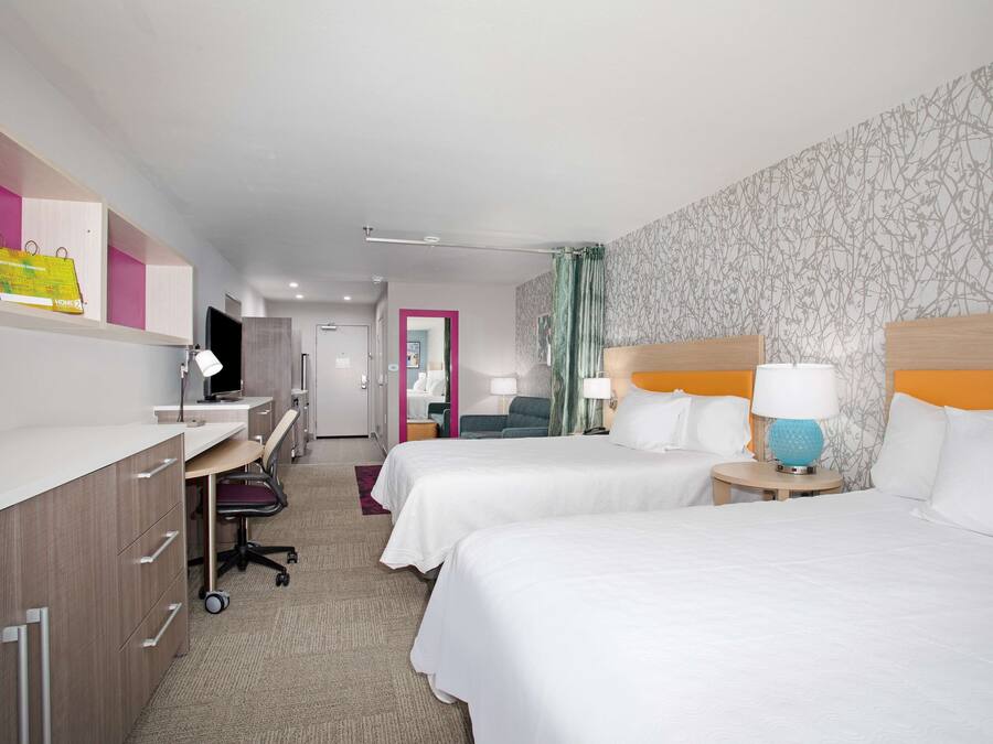 A hotel room with two beds, a desk with a computer, a chair, and a small table with a lamp.