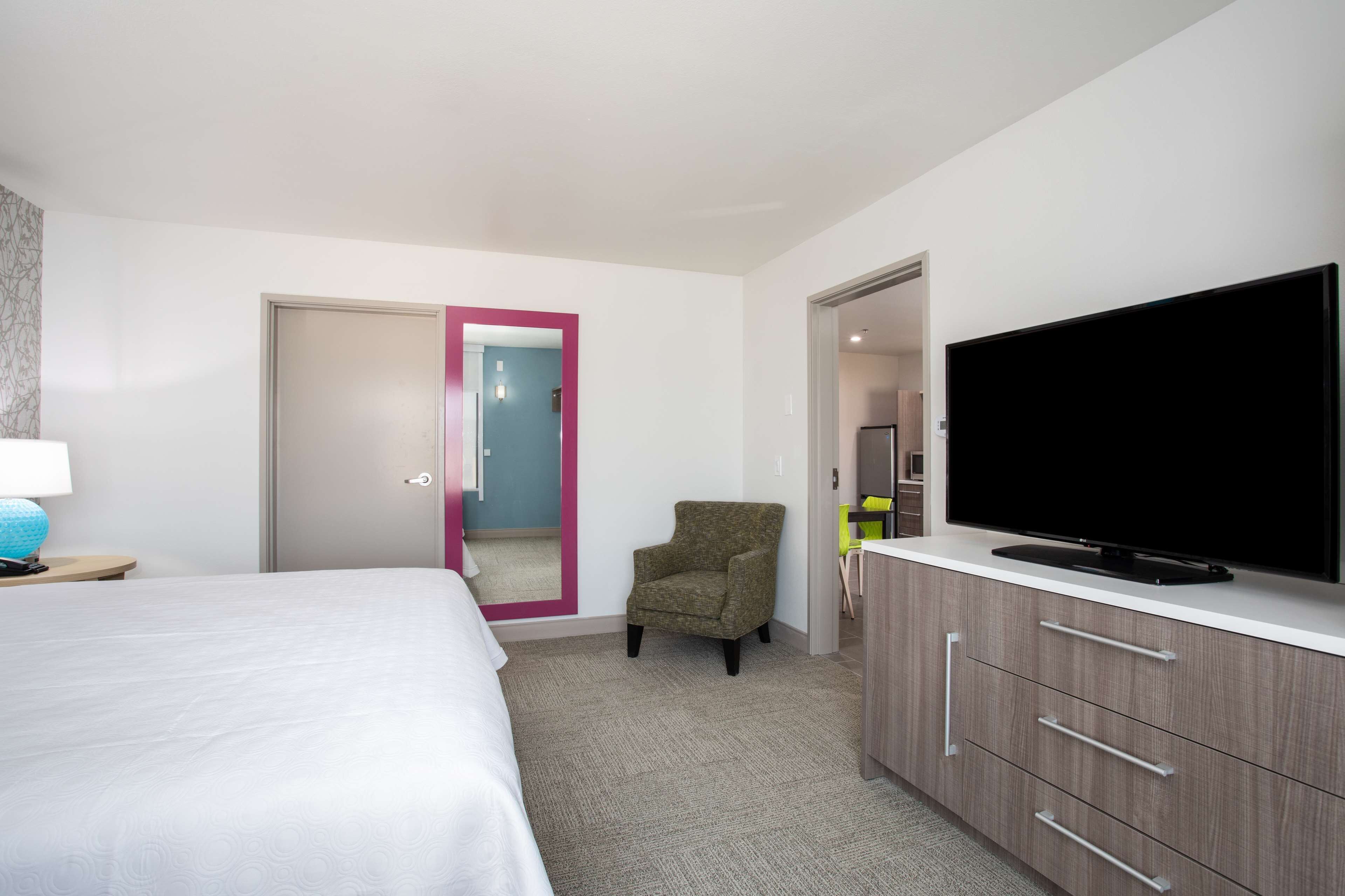 Una habitación de hotel con una cama, un televisor en un mueble, una silla y una puerta que da a otra habitación.