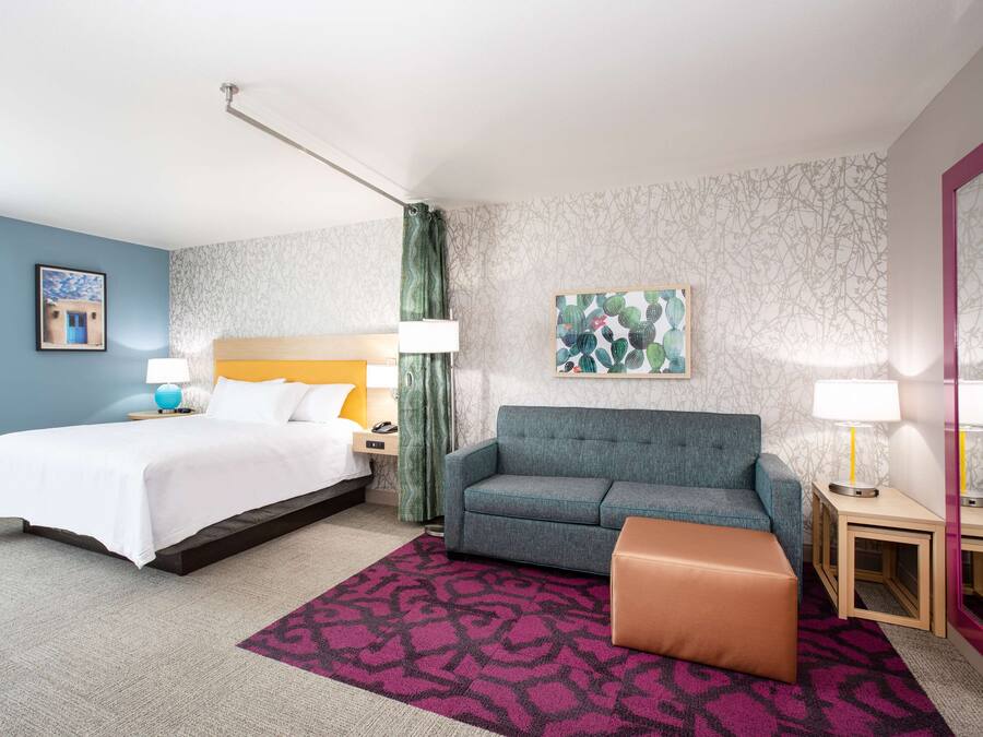 Una habitación de hotel con cama, sofá, una mesita y un buró.