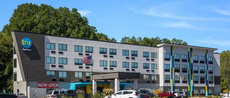 A hotel with a 'NOW OPEN' sign, multiple parking spaces, and a flag.