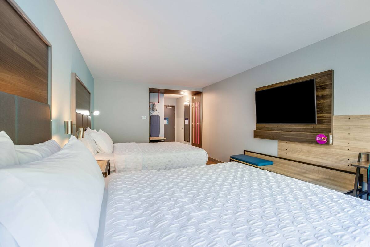 Une chambre d’hôtel avec deux lits, une télévision et une salle de bain visible à travers une porte ouverte.