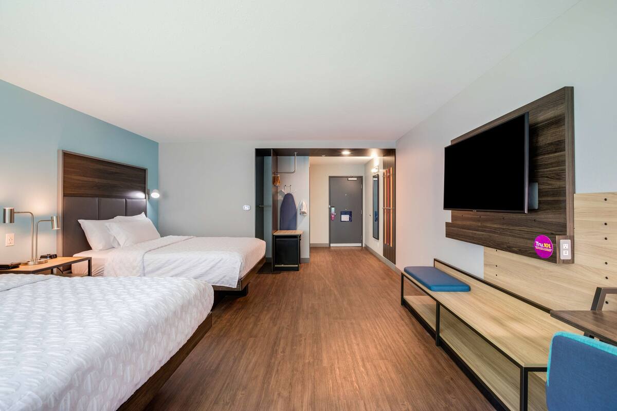Une chambre d’hôtel avec deux lits, un bureau, une télévision et une salle de bain visible à travers une porte ouverte.