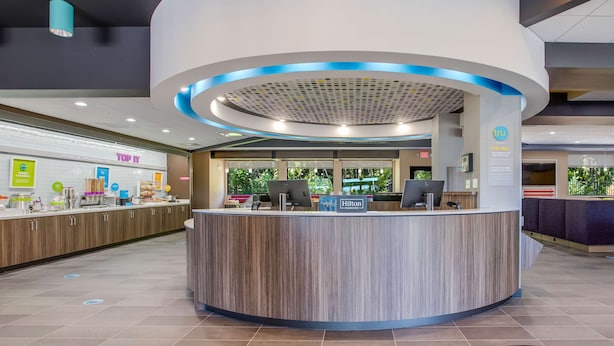 Een moderne hotel receptie met een gebogen balie, een groot raam met uitzicht op groen en een bordje met 'Hilton Honors'.