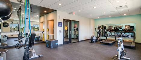 A modern gym with exercise equipment, a reception area, and a glass door entrance.