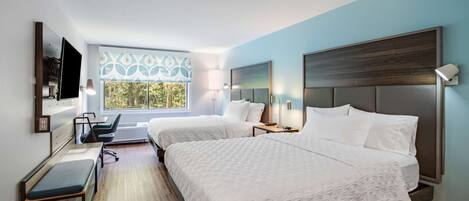 Ett modernt hotellrum med två sängar, ett skrivbord och ett stort fönster med dekorativa gardiner.