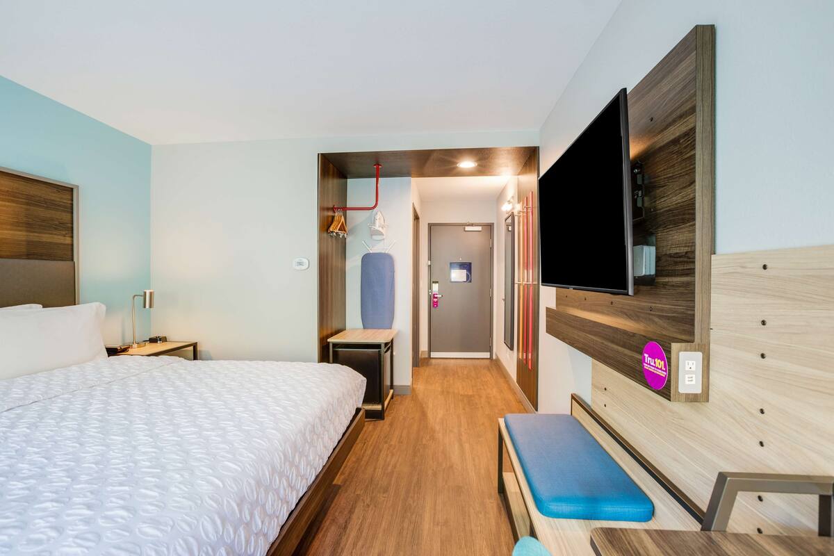 Une chambre d’hôtel avec un grand lit, un banc, une télévision et une tête de lit en bois.