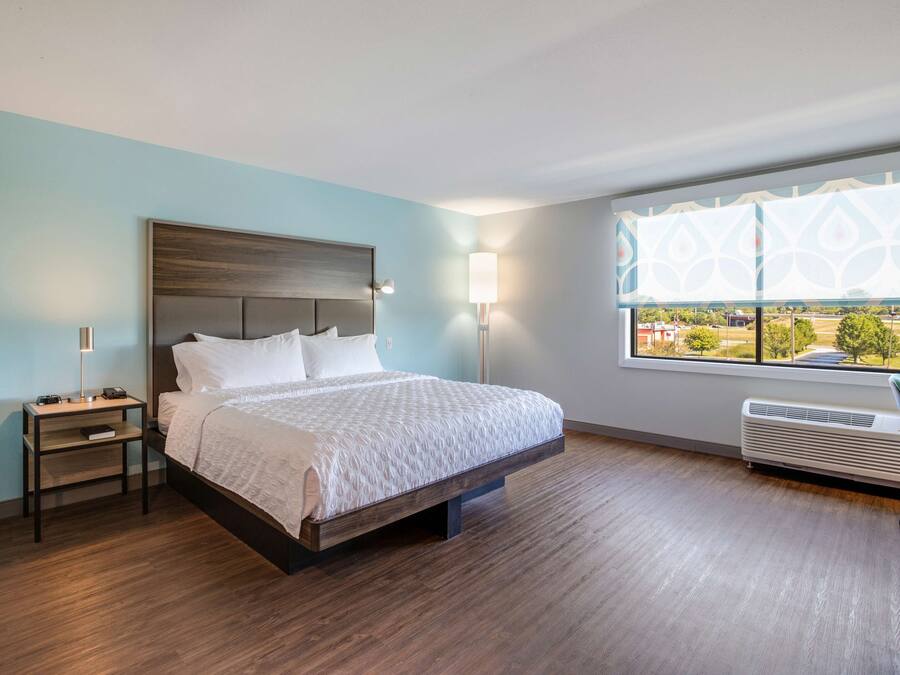 A hotel room with a large bed, bedside tables, a window with a view, and a wall-mounted air conditioner.
