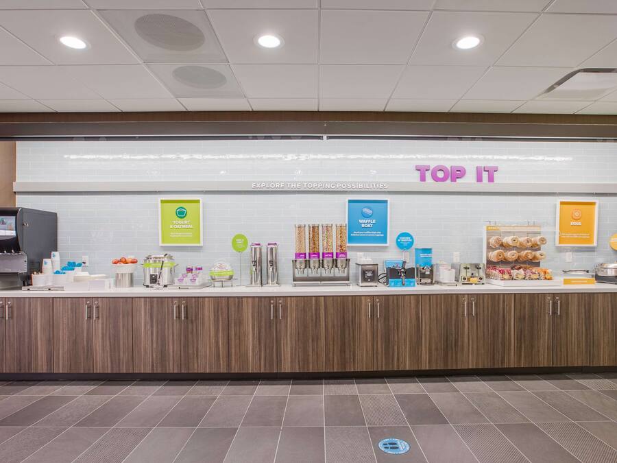 Un espace de petit-déjeuner en libre-service proposant une variété d’aliments et de boissons, notamment des yaourts, des gaufres et des œufs.